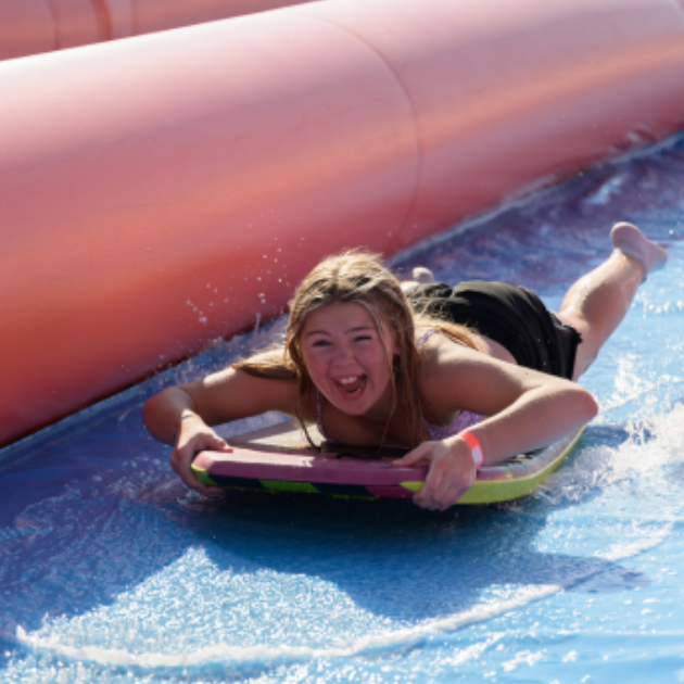 Child sliding down a water slide on a body board.