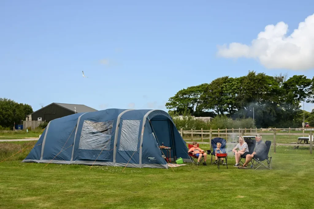 Family relaxing outside their tent on a camping pitch at Atlantic Reach
